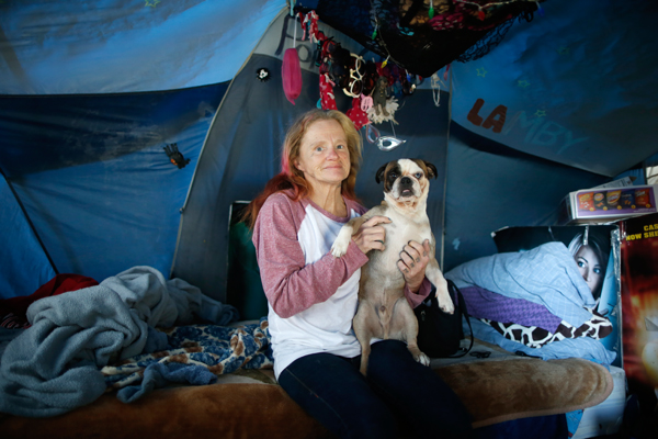 Kathleen Fox, 54, poses for a portrait with her dog Pork Chop by the tent in which she lives, under a freeway on a street in Los Angeles, California, United States, November 13, 2015. She has been living under the freeway for fourteen months to move away from the drugs that consumed the previous 30 years of her life. Los Angeles officials in September declared the rising problem of homelessness an "emergency" in the city and proposed spending $100 million to provide permanent housing and shelters to help the city's 26,000 indigent. The nation's second-largest city has nearly 18,000 individuals living on the streets, as opposed to shelters. REUTERS/Lucy Nicholson